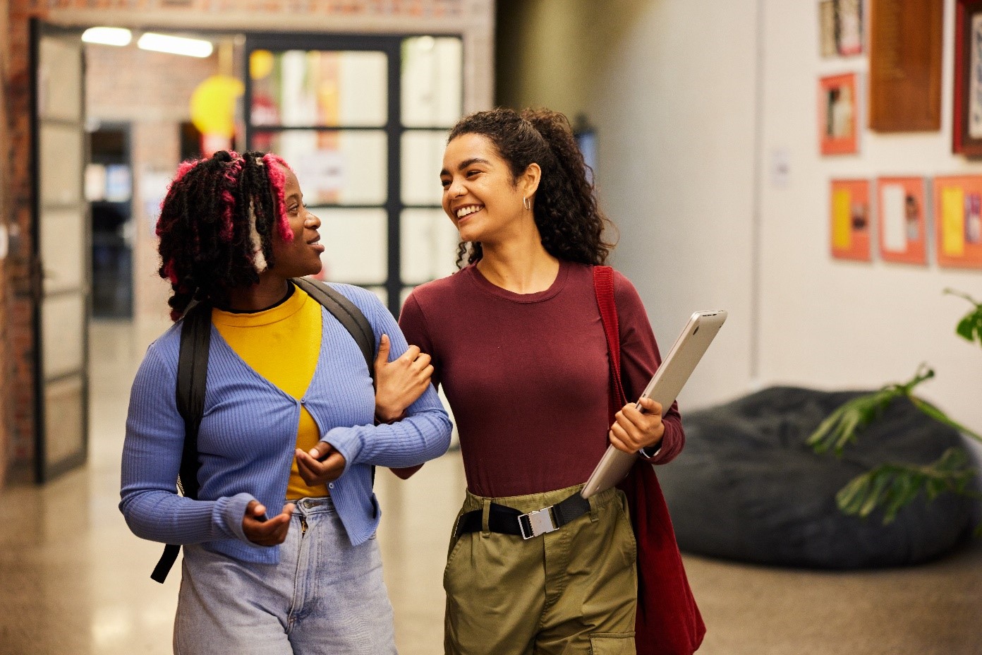 two women, smiling, arm in arm, one carrying a laptop