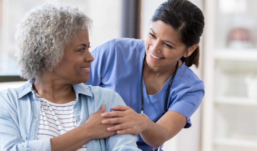 A seated older adult patient looks over her shoulder at a caregiver.