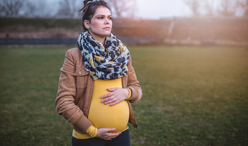 Pregnant woman standing in a park with her hands on her belly