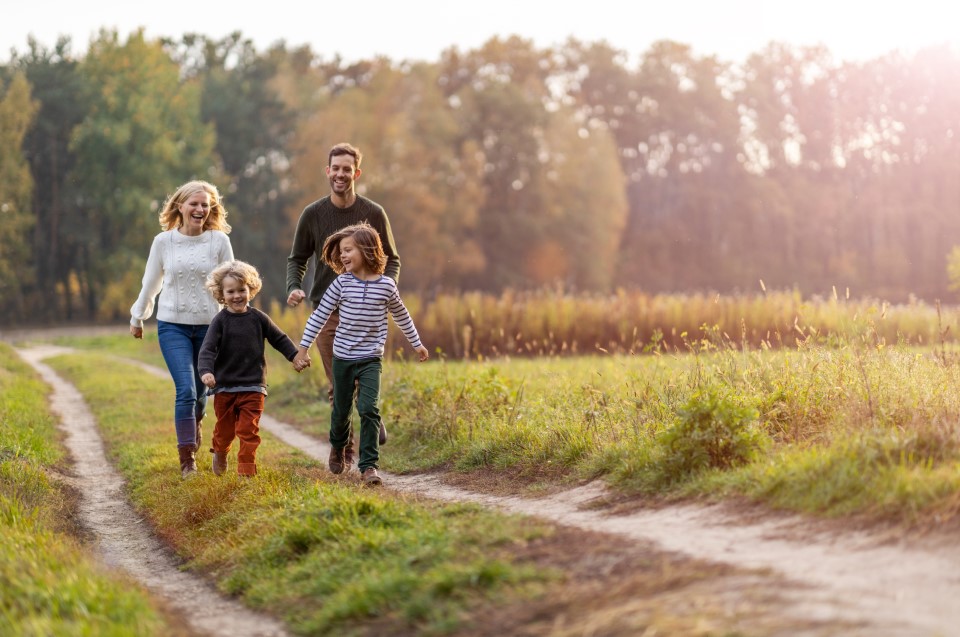 A family walking together along a grassy path in a sunlit field with trees in the background 