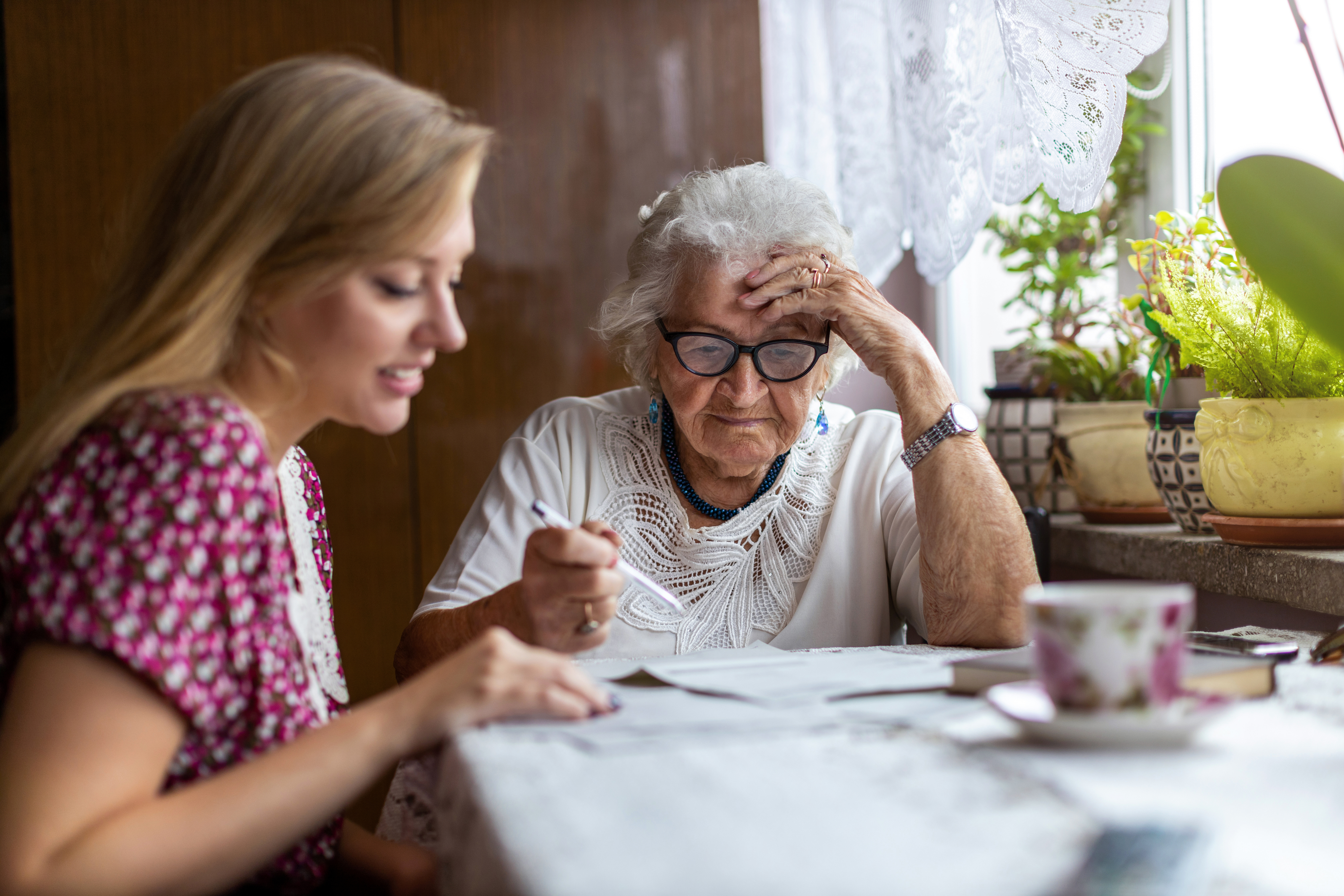Woman and Elderly Woman with pen in hand sitting at a table looking at some papers