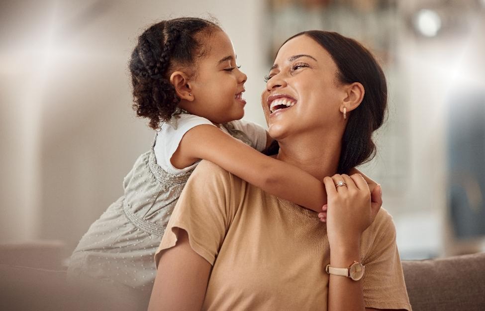 Daughter and mother smiling at each other as daughter hugs mother's shoulders from behind