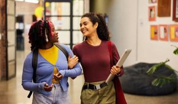 two women, smiling, arm in arm, one carrying a laptop