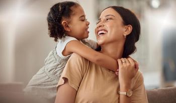 Daughter and mother smiling at each other as daughter hugs mother's shoulders from behind